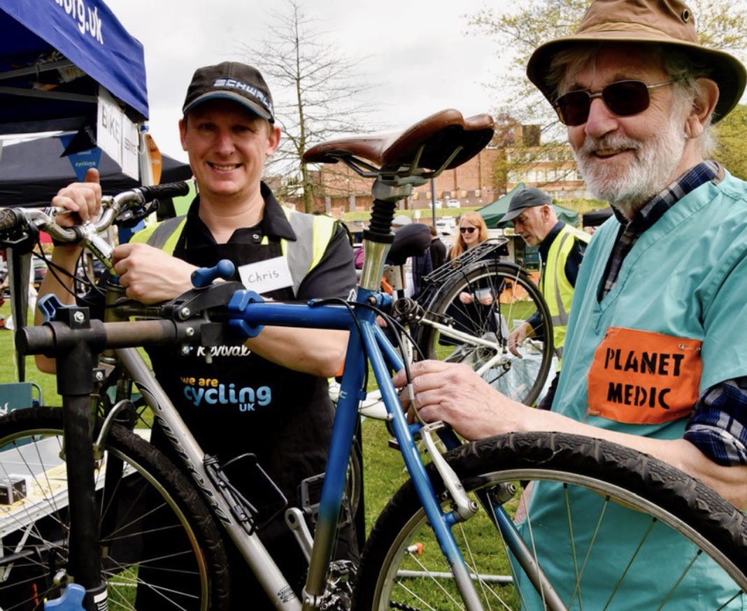 Background image to the find out about upcoming events link, featuring two people fixing a bicycle at the 2023 Fun Day event